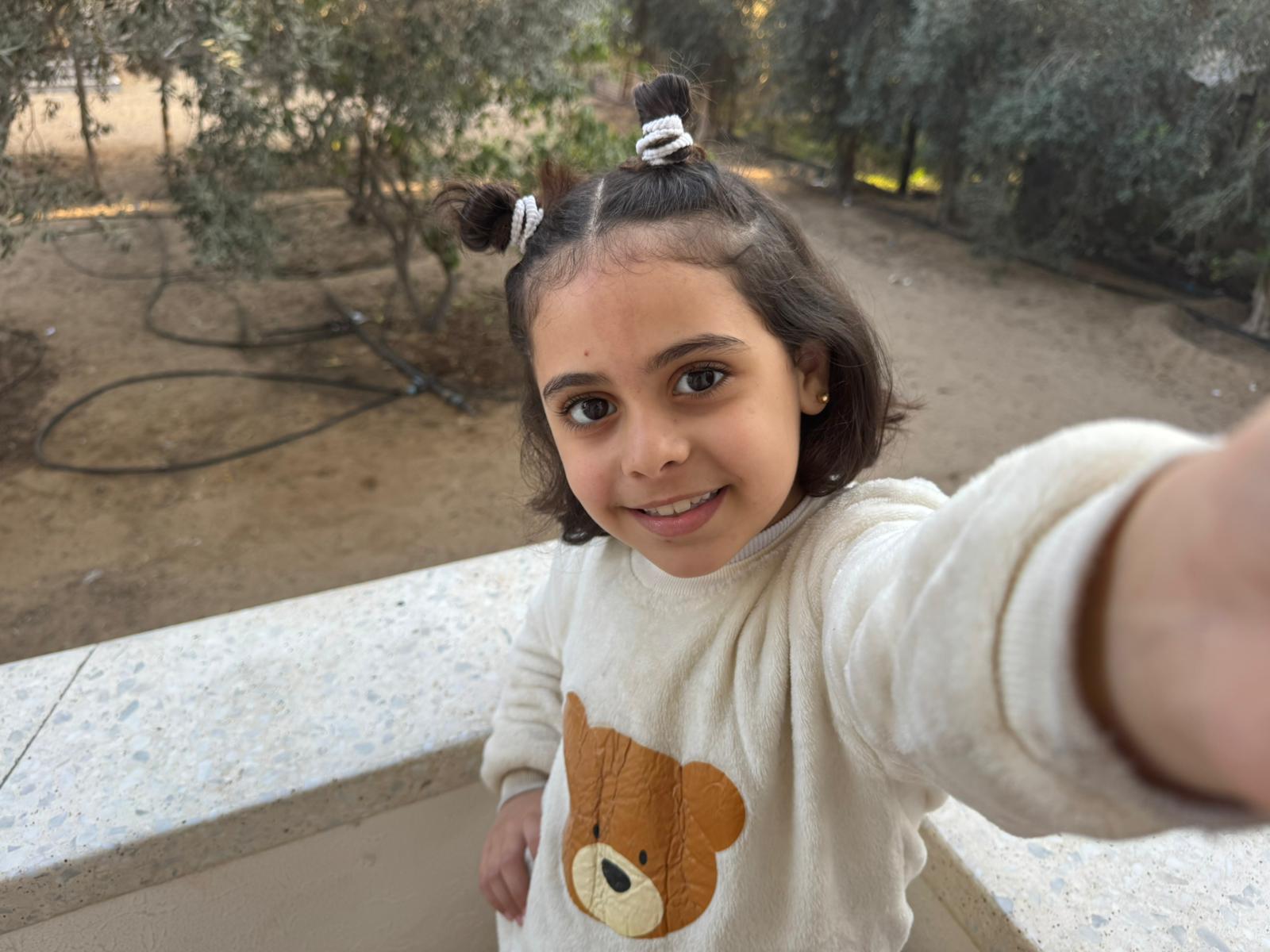 A young girl wearing a sweater with a teddy bear on it takes a selfie 